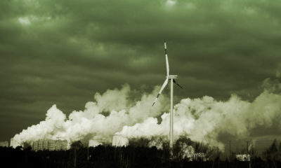 a single wind turbine spins next to exhaust from a coal-fired industrial plant
